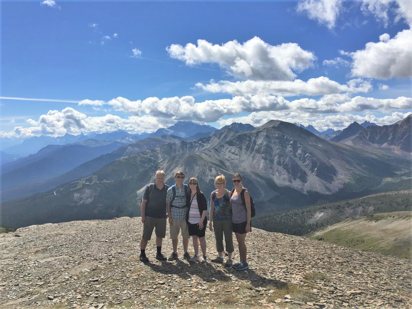 a group of five people (white) standing at the top of the Jasper Skyline mountain area with mountains in the background.